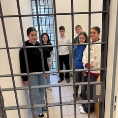 4 Mädchen und 2 Jungs lächelnd hinter einer Zellentür